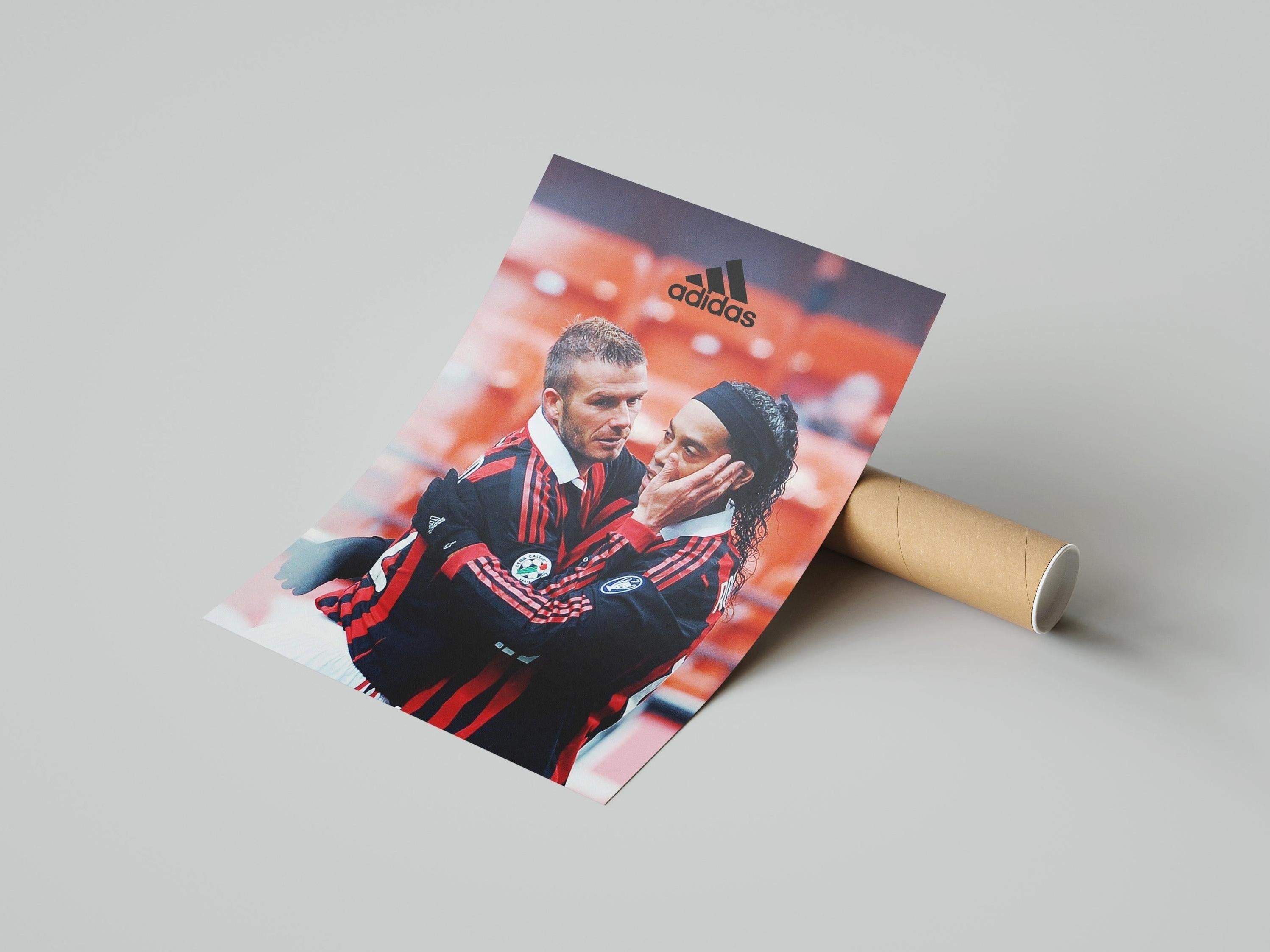 The Retro1999 Ronaldinho x David Beckham Poster shows both soccer stars in red and black Adidas jackets, standing close with one gently holding the others face. The Adidas logo appears at the top—a collectible for any football fan.