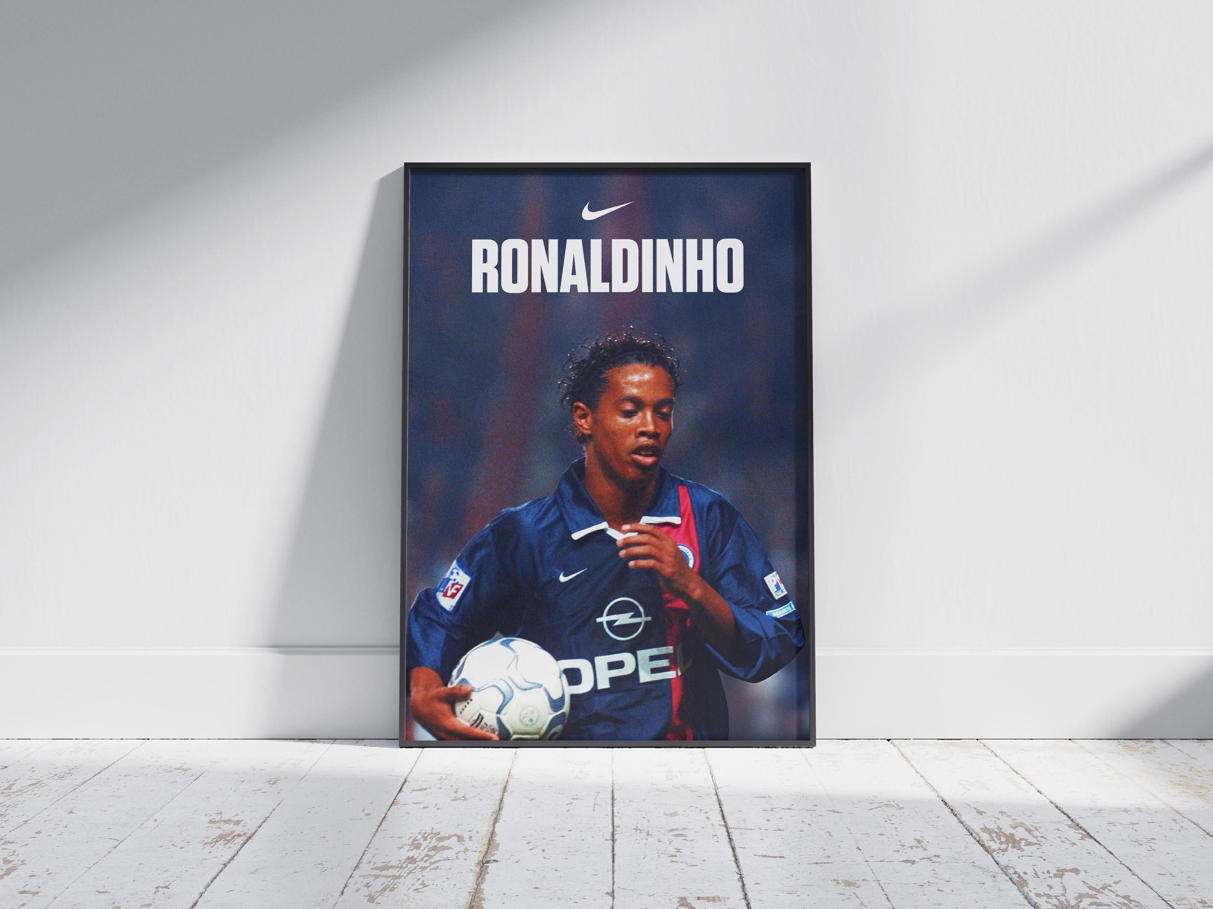 The Ronaldinho X PSG Poster by Retro1999 features PSG legend Ronaldinho in a blue and red jersey holding a ball, with “RONALDINHO” and the Nike logo above—perfect football memorabilia. Sunlight casts shadows on the wooden floor behind.