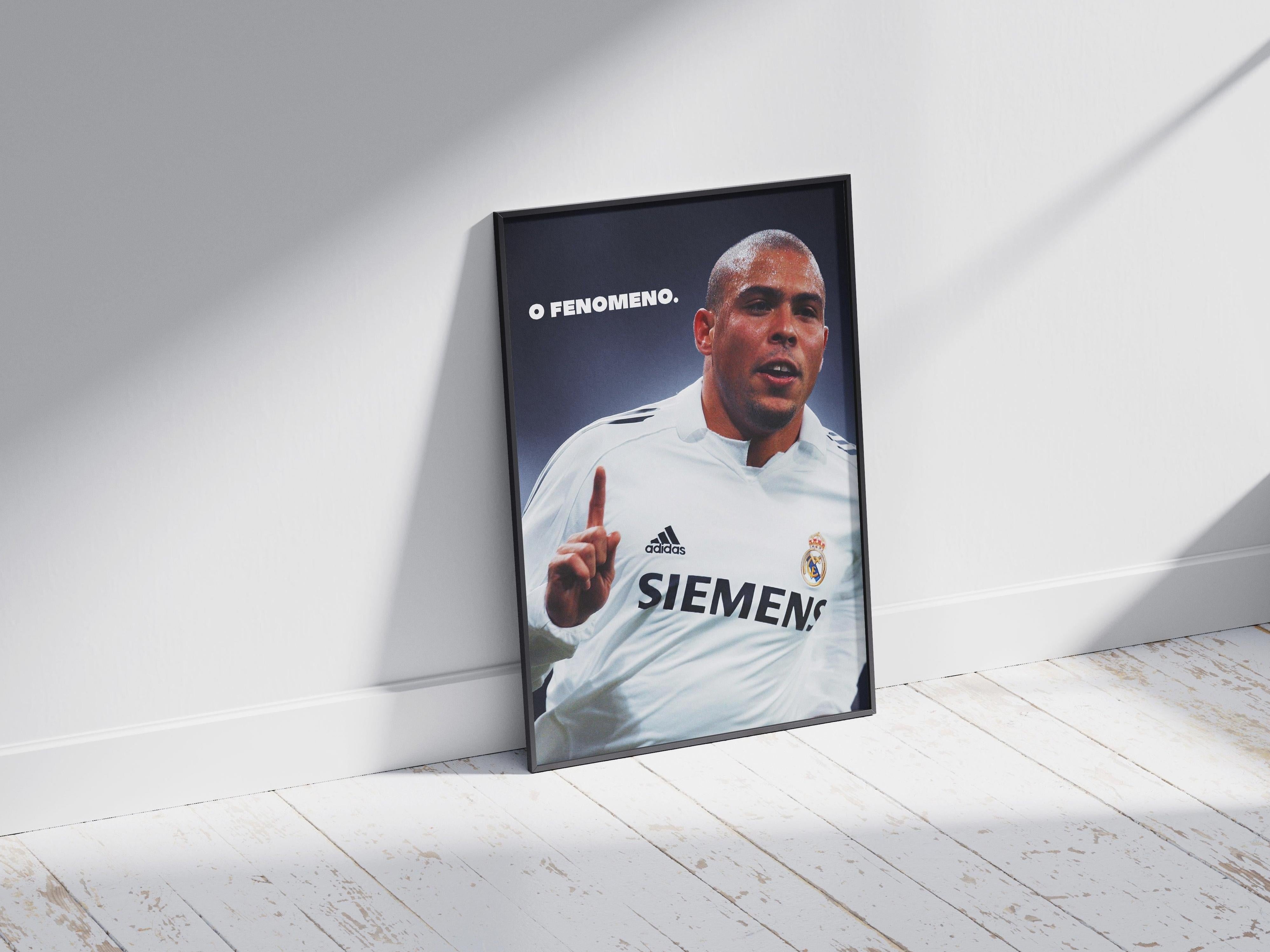 The Retro1999 Ronaldo O Fenômeno Poster features Ronaldo in a white Real Madrid jersey with O FENOMENO text, framed and set against a white wall on a light wooden floor, with sunlight evoking the Santiago Bernabeu atmosphere.