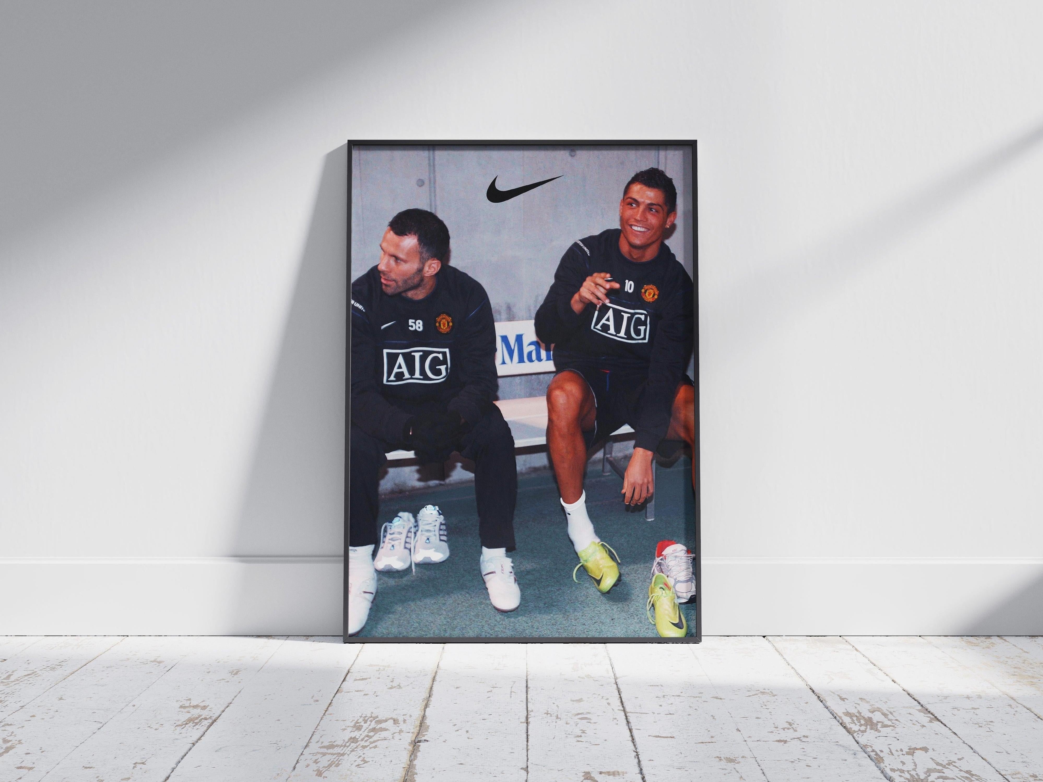 The Ryan Giggs x Cristiano Ronaldo Poster by Retro1999 features the Manchester United legends sitting on a bench in black AIG-branded training gear, smiling and talking under a Nike logo.