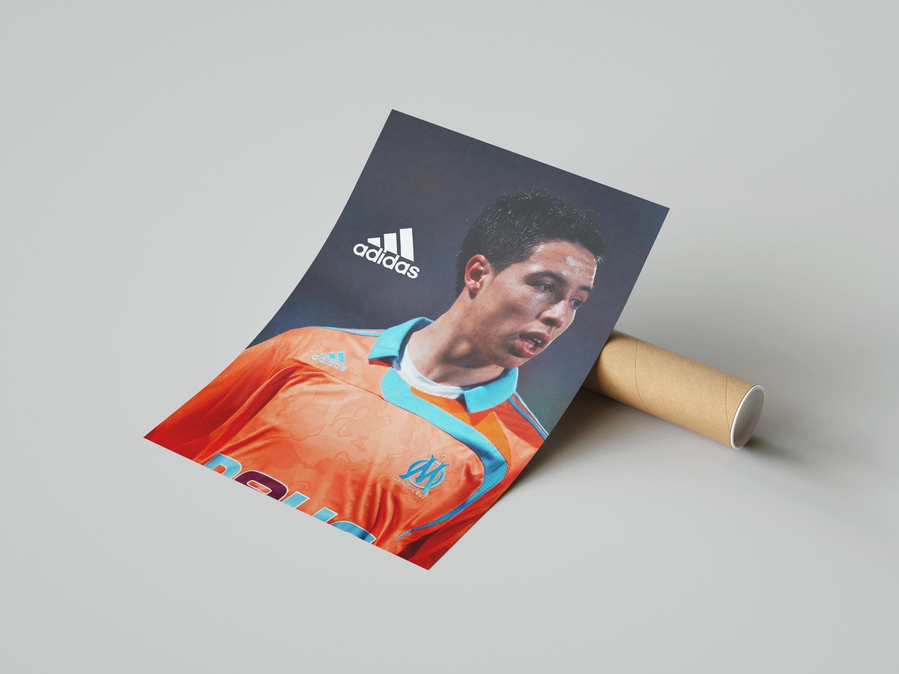 The Retro1999 Samir Nasri Marseille Poster, featuring him in an orange and blue Adidas jersey, is shown rolled on a light gray surface—a must-have football collectible for fans.