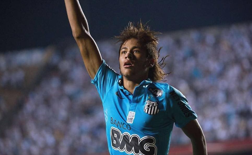 A soccer player in the Retro1999 Santos 2012-13 Third Shirt celebrates with one arm raised on the pitch, with a blurred crowd in the background.