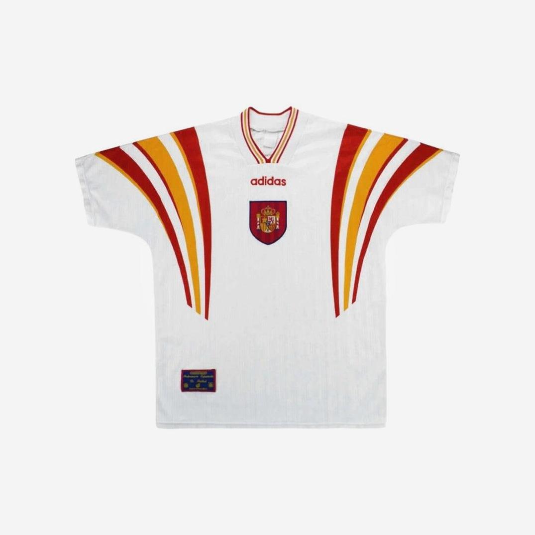 The Retro1999 Spain 1996 Away Shirt features white fabric, red and yellow curved shoulder stripes, a central national crest, and a bottom hem patch—a classic retro kit for dedicated soccer fans.