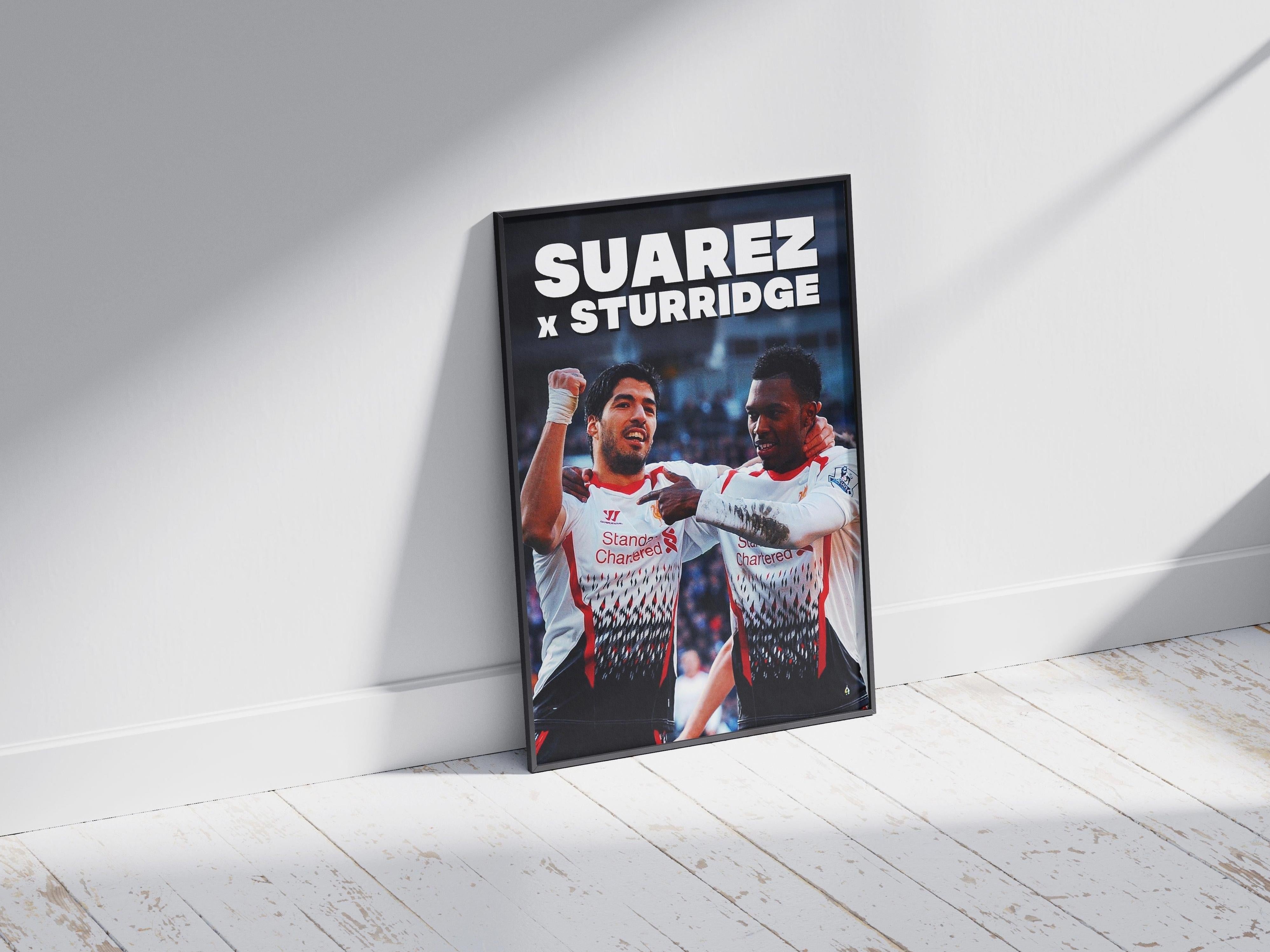The Retro1999 Sturridge x Suarez Poster features two soccer players in white kits celebrating under bold SUAREZ x STURRIDGE text. Framed and set on a wooden floor with sunlight, its perfect memorabilia for fans.