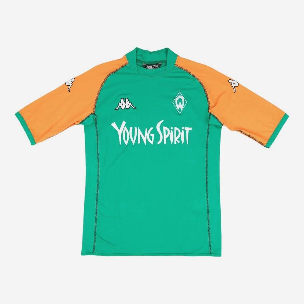 The Retro1999 Werder Bremen 2003-04 Home Shirt is a green and orange soccer jersey with Young Spirit front sponsor, Kappa logos on the shoulders, and a Werder Bremen crest. This retro kit features short sleeves and a simple collar.